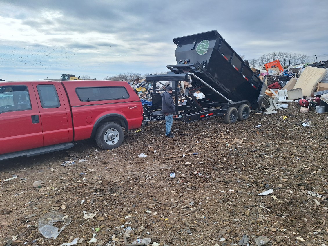 Dump trailer unloading waste at a littered outdoor disposal site
