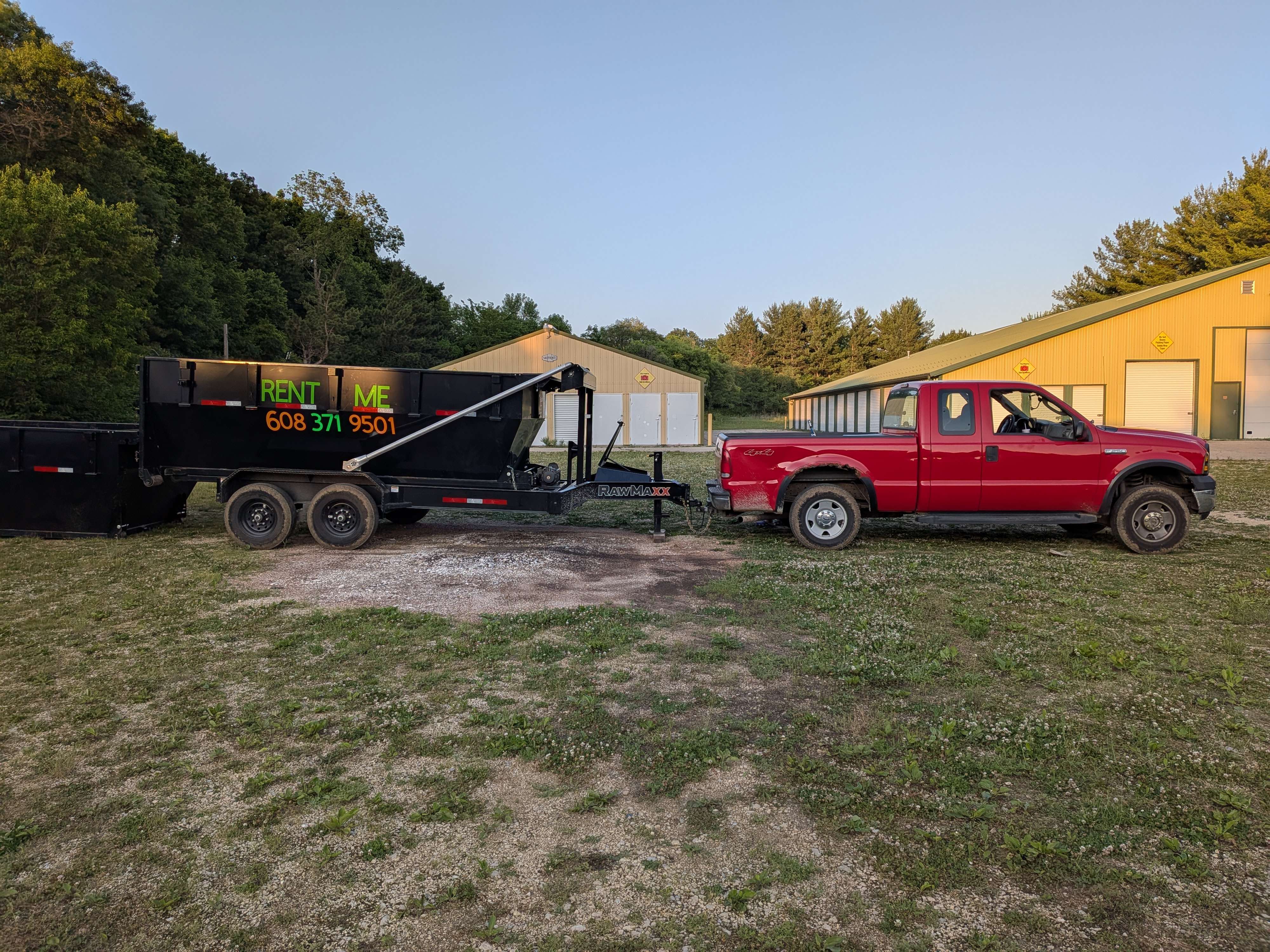 Black rental dumpster next to red pickup truck near yellow buildings
